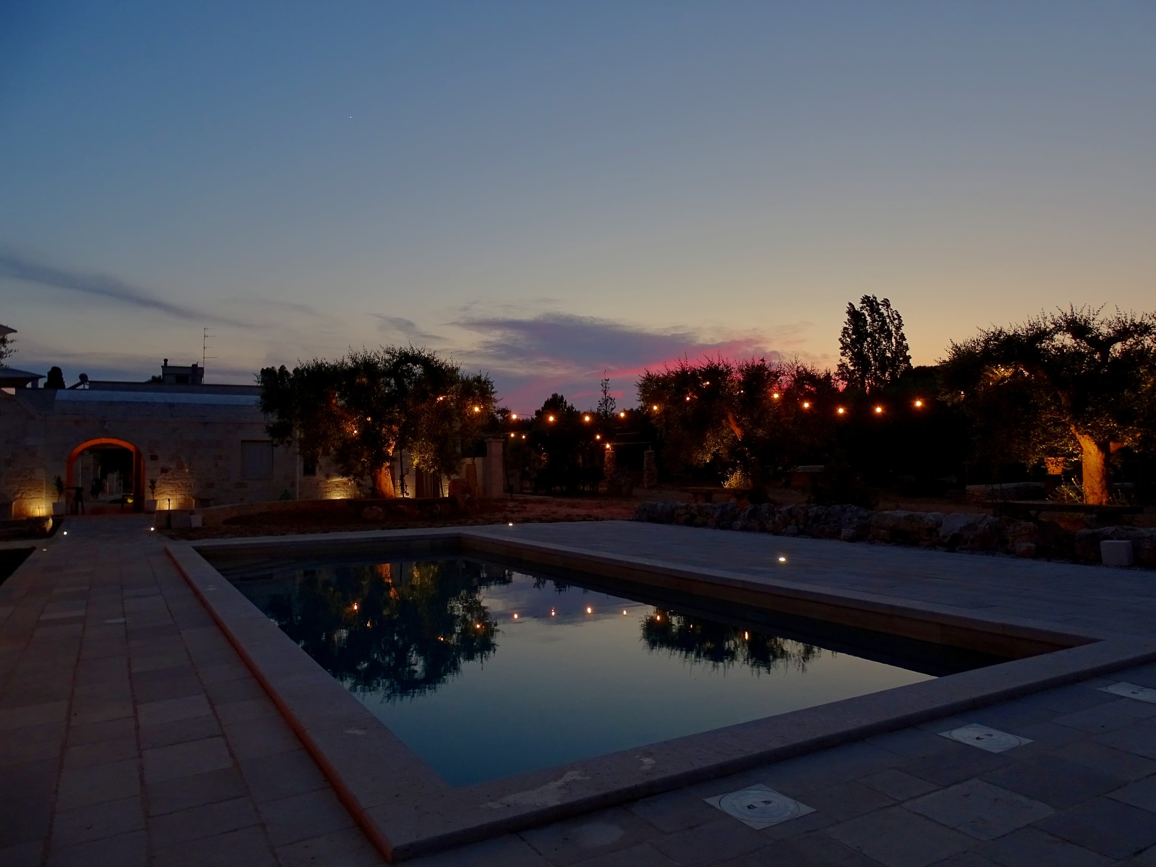 Piscina al tramonto con luci tra gli ulivi